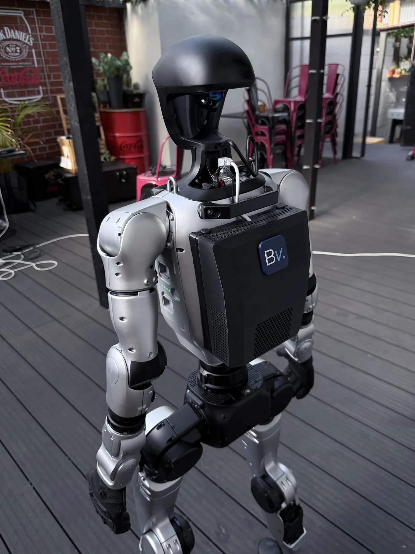 A Unitree G1 robot with the Botversity Voice backpack mounted, seen from the back